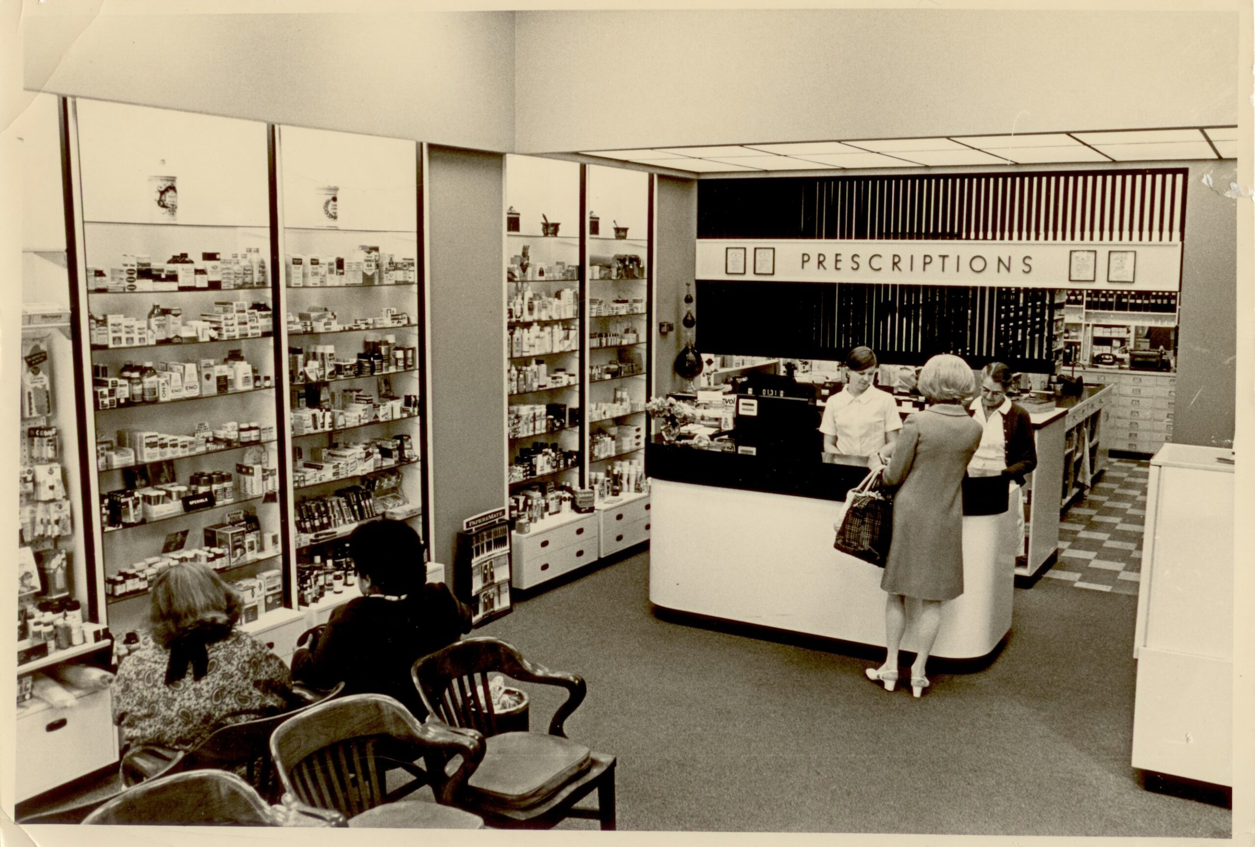 Interior of Macdonald's Prescriptions in 1971. Woman at a desk speaking with a pharmacist.