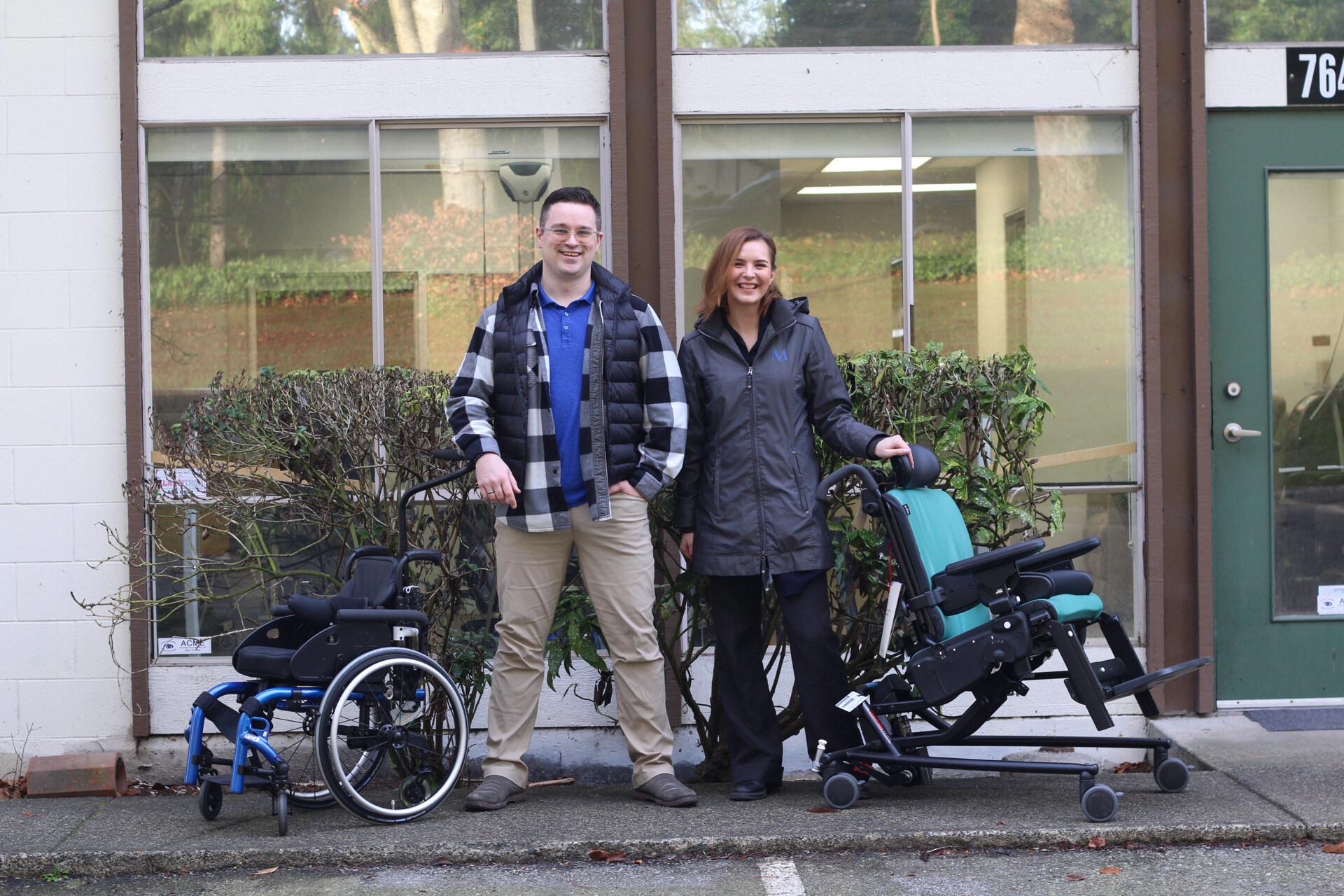 Luke and Anastasiia pose by two pediatric wheelchairs